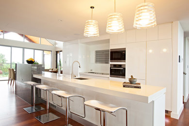 Foto på ett mellanstort kök, med en undermonterad diskho, vita skåp, bänkskiva i kvarts, vitt stänkskydd, glaspanel som stänkskydd, rostfria vitvaror, mellanmörkt trägolv och en köksö