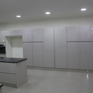 Idées déco pour une très grand cuisine moderne en U fermée avec un évier 3 bacs, un placard à porte plane, des portes de placard grises, un plan de travail en granite, une crédence beige, une crédence en carreau de porcelaine, un électroménager en acier inoxydable, un sol en carrelage de céramique, un îlot central, un sol beige et un plan de travail noir.