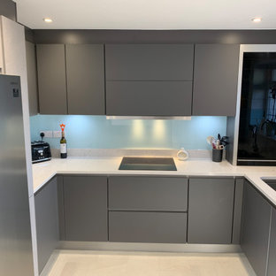 Design ideas for a mid-sized contemporary u-shaped separate kitchen in Sussex with an undermount sink, flat-panel cabinets, grey cabinets, quartzite benchtops, blue splashback, glass sheet splashback, black appliances, vinyl floors, a peninsula, beige floor and grey benchtop.