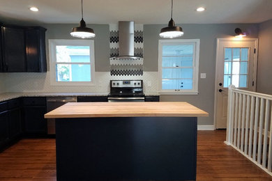 Example of a minimalist l-shaped dark wood floor and brown floor open concept kitchen design in Minneapolis with an undermount sink, shaker cabinets, blue cabinets, granite countertops, white backsplash, mosaic tile backsplash, stainless steel appliances and an island