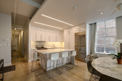 Example of a mid-sized trendy l-shaped kitchen design in New York with an undermount sink, flat-panel cabinets, white cabinets, quartzite countertops, beige backsplash, stainless steel appliances and an island