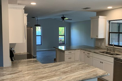 Inspiration for a mid-sized transitional galley medium tone wood floor and brown floor enclosed kitchen remodel in Tampa with a double-bowl sink, shaker cabinets, white cabinets, granite countertops, stainless steel appliances, a peninsula and brown countertops