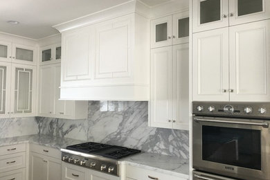 Foto på ett stort vintage vit kök, med en undermonterad diskho, luckor med profilerade fronter, vita skåp, marmorbänkskiva, vitt stänkskydd, stänkskydd i sten, rostfria vitvaror, mörkt trägolv och brunt golv