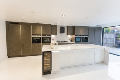 Large modern galley open plan kitchen in London with an integrated sink, flat-panel cabinets, brown cabinets, engineered stone countertops, black appliances, an island and white worktops.