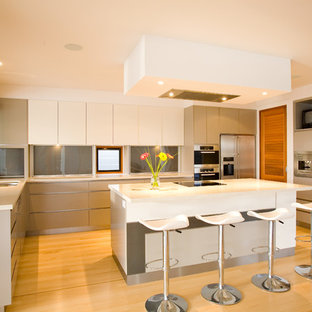 This is an example of a large contemporary l-shaped kitchen in Sunshine Coast with flat-panel cabinets, stainless steel appliances, light hardwood floors, white benchtop, an undermount sink, grey splashback, glass sheet splashback, with island, beige floor and white cabinets.