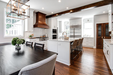 Large transitional u-shaped medium tone wood floor, brown floor and exposed beam enclosed kitchen photo in Atlanta with an undermount sink, beaded inset cabinets, white cabinets, quartz countertops, white backsplash, subway tile backsplash, stainless steel appliances, an island and gray countertops