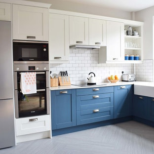 Photo of a mid-sized contemporary u-shaped eat-in kitchen in Other with a farmhouse sink, shaker cabinets, blue cabinets, recycled glass benchtops, white splashback, ceramic splashback, linoleum floors, a peninsula and grey floor.