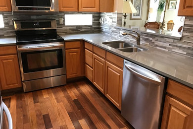 Mid-sized trendy u-shaped medium tone wood floor and brown floor enclosed kitchen photo in Denver with an undermount sink, raised-panel cabinets, medium tone wood cabinets, quartz countertops, metallic backsplash, glass tile backsplash, stainless steel appliances, no island and gray countertops