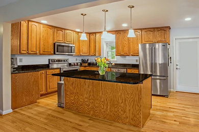 Elegant l-shaped medium tone wood floor open concept kitchen photo in Baltimore with a double-bowl sink, raised-panel cabinets, medium tone wood cabinets, granite countertops, stainless steel appliances and an island