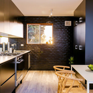 Inspiration for a beach style galley eat-in kitchen in Adelaide with an undermount sink, flat-panel cabinets, black cabinets, metallic splashback, mirror splashback, black appliances, light hardwood floors, no island, beige floor and white benchtop.