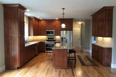 Classic l-shaped kitchen/diner in Boston with a double-bowl sink, shaker cabinets, dark wood cabinets, granite worktops, stainless steel appliances, light hardwood flooring and an island.