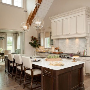 Foto de cocina comedor en L, tradicional, grande, con fregadero de un seno, armarios estilo shaker, puertas de armario beige, encimera de mármol, salpicadero blanco, salpicadero de azulejos de piedra, electrodomésticos con paneles, una isla y suelo de madera en tonos medios