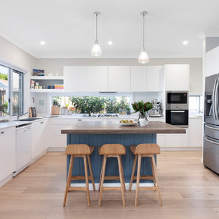 Inspiration for a contemporary u-shaped kitchen in Sydney with a double-bowl sink, flat-panel cabinets, white cabinets, wood benchtops, grey splashback, stainless steel appliances, medium hardwood floors, with island, beige floor and white benchtop.