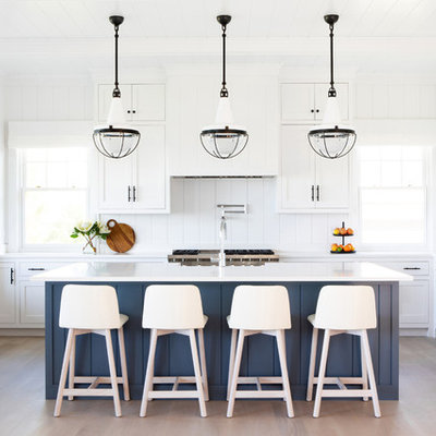 Large beach style u-shaped light wood floor and beige floor eat-in kitchen photo in New York with shaker cabinets, white cabinets, white backsplash, stainless steel appliances, an island, white countertops, a farmhouse sink, quartz countertops and wood backsplash