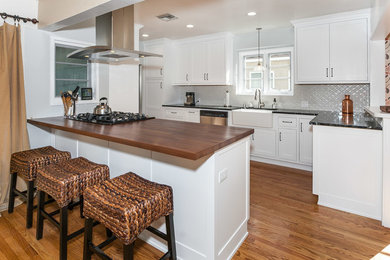 Mid-sized elegant eat-in kitchen photo in Los Angeles with a farmhouse sink, recessed-panel cabinets, white cabinets, gray backsplash, ceramic backsplash, stainless steel appliances, an island and soapstone countertops