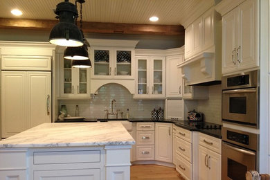 Large arts and crafts l-shaped light wood floor eat-in kitchen photo in Jackson with a farmhouse sink, raised-panel cabinets, white cabinets, soapstone countertops, white backsplash, subway tile backsplash, stainless steel appliances and an island