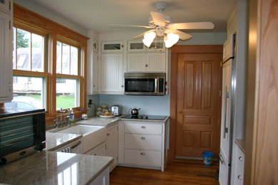 Example of a small arts and crafts u-shaped medium tone wood floor kitchen design in Other with a farmhouse sink, beaded inset cabinets, white cabinets, granite countertops, blue backsplash, paneled appliances and no island