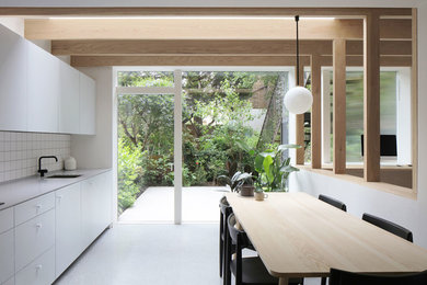 ロンドンにある北欧スタイルのおしゃれなダイニングキッチン (シングルシンク、フラットパネル扉のキャビネット、白いキャビネット、白いキッチンパネル、白い床、白いキッチンカウンター) の写真