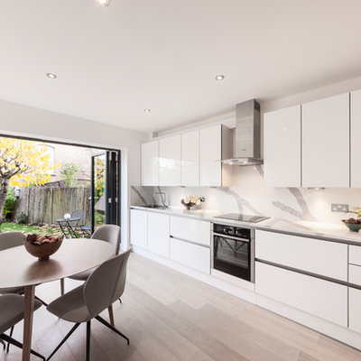 Example of a minimalist single-wall eat-in kitchen design in London with flat-panel cabinets, white cabinets, stainless steel appliances, no island and white countertops