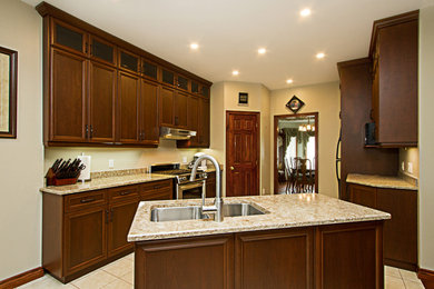 This is an example of a medium sized traditional galley kitchen/diner in Toronto with recessed-panel cabinets, dark wood cabinets, granite worktops, an island, a double-bowl sink, stainless steel appliances and ceramic flooring.