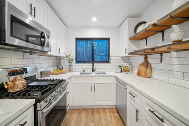 Small farmhouse galley kitchen/diner in San Diego with a double-bowl sink, flat-panel cabinets, white cabinets, marble worktops, white splashback, metro tiled splashback, stainless steel appliances, light hardwood flooring, an island, brown floors and white worktops.