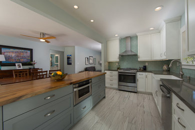 Example of a mid-sized beach style l-shaped porcelain tile eat-in kitchen design in San Diego with a farmhouse sink, shaker cabinets, white cabinets, quartz countertops, blue backsplash, subway tile backsplash, stainless steel appliances and an island
