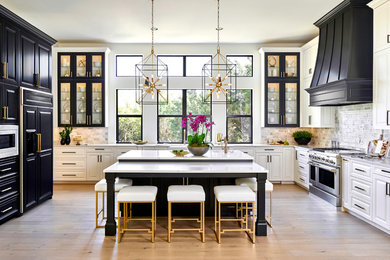Example of a transitional u-shaped light wood floor and beige floor kitchen design in Austin with a farmhouse sink, raised-panel cabinets, gray backsplash, paneled appliances, an island, white countertops, quartz countertops and white cabinets