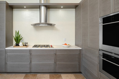 This is an example of a medium sized contemporary l-shaped open plan kitchen in Phoenix with flat-panel cabinets, grey cabinets, engineered stone countertops, white splashback, porcelain splashback, stainless steel appliances, travertine flooring and brown floors.