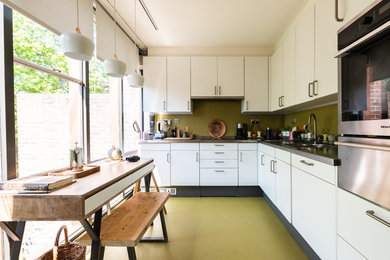 Medium sized midcentury l-shaped kitchen/diner in London with flat-panel cabinets, white cabinets, granite worktops, green splashback, stainless steel appliances, no island, green floors, black worktops and a double-bowl sink.