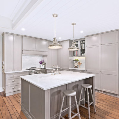 Transitional l-shaped medium tone wood floor and brown floor kitchen photo in Sydney with a farmhouse sink, recessed-panel cabinets, gray cabinets, white backsplash, stainless steel appliances, an island and white countertops