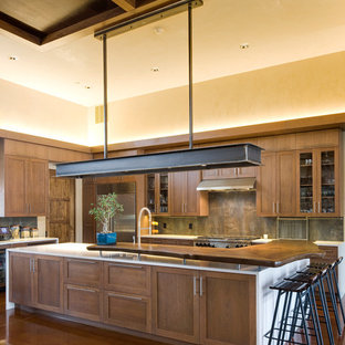 Photo of an expansive rustic l-shaped kitchen/diner in Albuquerque with shaker cabinets, dark wood cabinets, wood worktops, multi-coloured splashback, stainless steel appliances, a submerged sink, stone tiled splashback, concrete flooring and an island.