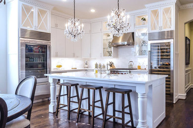 Inspiration for a mid-sized timeless l-shaped medium tone wood floor eat-in kitchen remodel in Dallas with a farmhouse sink, recessed-panel cabinets, white cabinets, marble countertops, gray backsplash, stone tile backsplash, stainless steel appliances and an island