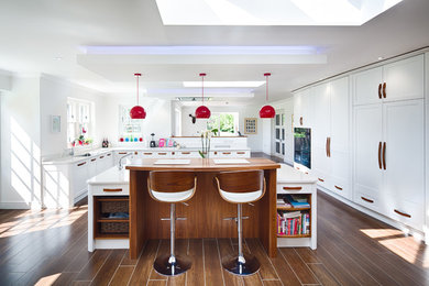 This is an example of an expansive contemporary u-shaped kitchen/diner in Other with a double-bowl sink, shaker cabinets, white cabinets, granite worktops, stainless steel appliances, porcelain flooring, an island, brown floors and white splashback.