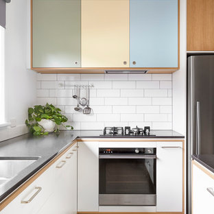 Foto de cocina de galera, escandinava, grande, con despensa, fregadero encastrado, armarios con rebordes decorativos, puertas de armario de madera oscura, encimera de cemento, salpicadero blanco, salpicadero de azulejos tipo metro, electrodomésticos de acero inoxidable, suelo de corcho y una isla