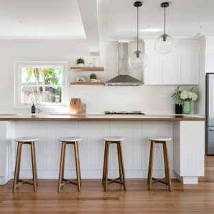 Design ideas for a beach style open plan kitchen in Sydney with a farmhouse sink, white cabinets, wood benchtops, white splashback, subway tile splashback, stainless steel appliances and with island.