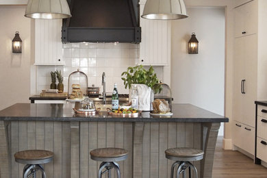 Large transitional u-shaped medium tone wood floor and brown floor open concept kitchen photo with a farmhouse sink, flat-panel cabinets, white cabinets, granite countertops, white backsplash, ceramic backsplash, stainless steel appliances, an island and black countertops