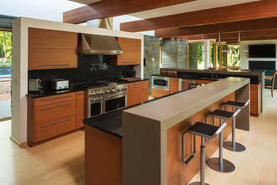 Example of a trendy galley light wood floor eat-in kitchen design in Other with light wood cabinets, solid surface countertops, black backsplash, stone slab backsplash, stainless steel appliances and two islands