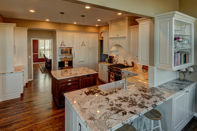 Example of a mid-sized classic u-shaped medium tone wood floor eat-in kitchen design in Denver with a farmhouse sink, raised-panel cabinets, white cabinets, granite countertops, white backsplash, ceramic backsplash, stainless steel appliances and an island