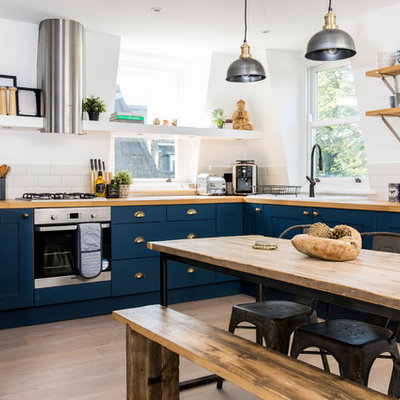 Example of a mid-sized trendy u-shaped light wood floor and beige floor eat-in kitchen design in London with recessed-panel cabinets, blue cabinets, wood countertops and stainless steel appliances