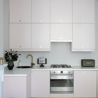 Exemple d'une cuisine tendance en L avec un évier posé, un placard à porte plane, des portes de placard violettes, une crédence blanche, un électroménager en acier inoxydable, un sol gris et un plan de travail blanc.