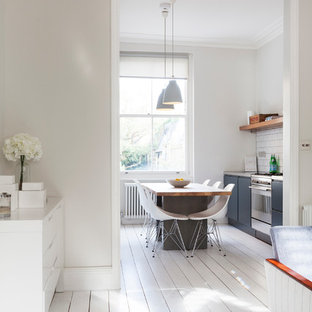 Photo of a small scandinavian galley eat-in kitchen in London with flat-panel cabinets, grey cabinets, white splashback, subway tile splashback, stainless steel appliances, painted wood floors, with island and white floor.