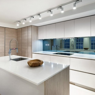 This is an example of a large contemporary l-shaped kitchen/diner in London with a submerged sink, flat-panel cabinets, white cabinets, mirror splashback, black appliances, an island, beige floors, white worktops, composite countertops, metallic splashback and limestone flooring.