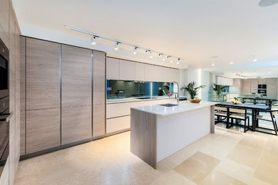 Photo of a large contemporary l-shaped kitchen/diner in London with a submerged sink, flat-panel cabinets, white cabinets, composite countertops, metallic splashback, mirror splashback, black appliances, limestone flooring, an island, beige floors and white worktops.