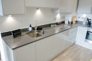 Photo of a medium sized modern l-shaped enclosed kitchen in London with a built-in sink, flat-panel cabinets, white cabinets, granite worktops, grey splashback, stainless steel appliances, no island and grey worktops.