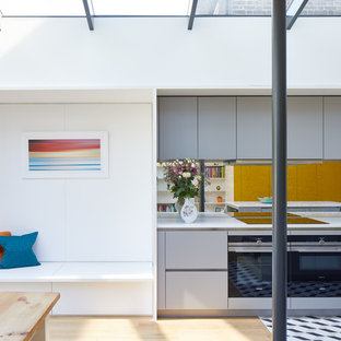 Contemporary kitchen/diner in London with flat-panel cabinets, grey cabinets, mirror splashback, an island, multi-coloured floors and white worktops.