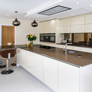 Inspiration for a large contemporary galley kitchen in Hertfordshire with flat-panel cabinets, metallic splashback, mirror splashback, stainless steel appliances, slate flooring, brown worktops, a submerged sink, beige cabinets, an island and white floors.