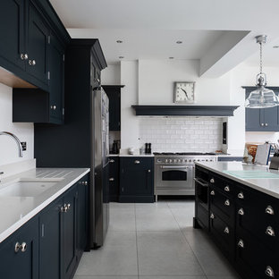 Design ideas for a traditional l-shaped kitchen in Hertfordshire with a submerged sink, beaded cabinets, black cabinets, white splashback, metro tiled splashback, stainless steel appliances, an island, grey floors and white worktops.
