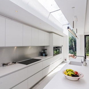 Photo of a large modern single-wall eat-in kitchen in London with an integrated sink, flat-panel cabinets, white cabinets, solid surface benchtops, white splashback, stainless steel appliances, porcelain floors and a peninsula.