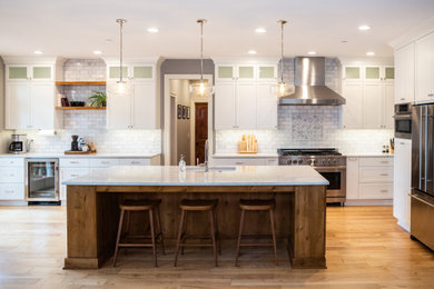 Example of a transitional medium tone wood floor and brown floor open concept kitchen design in Portland with an undermount sink, shaker cabinets, white cabinets, multicolored backsplash, subway tile backsplash, stainless steel appliances, an island and multicolored countertops