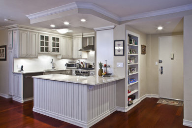 Inredning av ett modernt litet kök, med en enkel diskho, luckor med upphöjd panel, vita skåp, vitt stänkskydd, rostfria vitvaror, mörkt trägolv och en halv köksö